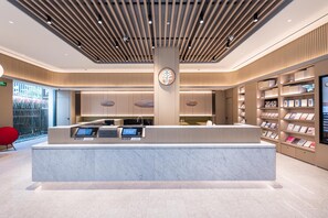A modern reception desk with digital displays, a central pillar with a clock, and a book-filled bookshelf to the right. - Ji Hotel (nanjing Xinjiekou Central Shopping Cente (Nanjing)