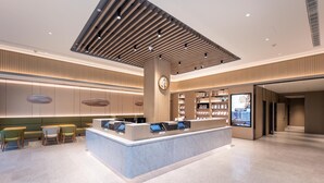 En moderne hotellobby med reception, siddeområde og et stort digitalt display.