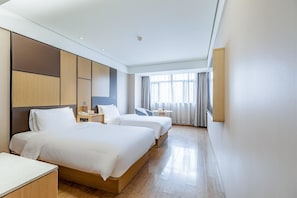 Habitació d'hotel amb dos llits, una taula de treball, una cadira, una taula petita i una finestra amb cortines.