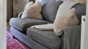 Ein Wohnzimmer mit grauem Sofa, weißen, flauschigen Kissen, einer Lampe und einer Steinwand.