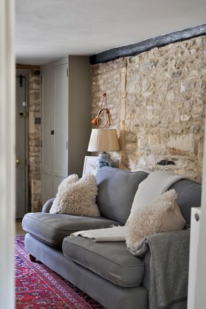 Ein Wohnzimmer mit grauem Sofa, weißen, flauschigen Kissen, einer Lampe und einer Steinwand.