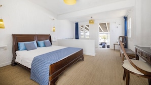 A bedroom with a wooden bed, a desk, and a chair. There is a window with blue curtains and a view of the outdoors. - Lassion Beach Hotel (Sitia)
