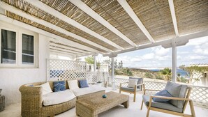 A covered outdoor seating area with wicker furniture and a view of the sea. - Lassion Beach Hotel (Sitia)