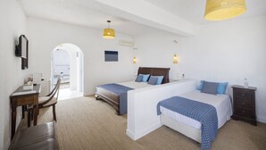 A hotel room with two beds, a desk, and a chair. There is a large window and a door leading outside. - Lassion Beach Hotel (Sitia)