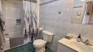 Un baño con inodoro, cortina de ducha, toallero y lavamanos con dispensador de jabón.