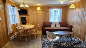 Una habitación con paneles de madera, un sofá, una mesa de centro, una mesa de comedor con sillas, una chimenea y un televisor.