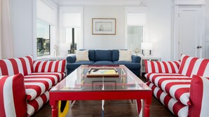 A modern living room with a blue sofa, red and white striped armchairs, a glass coffee table, and a framed picture on the wall.