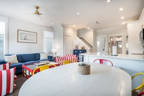 A modern living room with a sofa, a dining table, and a kitchen area in the background. - Newport at The Cove Riverwalk Villas (Wilmington)