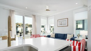 A modern kitchen with a central island, a dining area with striped chairs, and a view of the city.