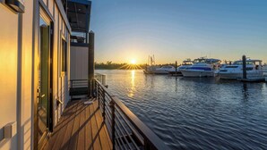 A waterfront property with a wooden deck, a glass door entrance, and boats docked in the background.