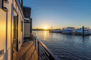 A waterfront property with a wooden deck, a glass door entrance, and boats docked in the background. - Newport at The Cove Riverwalk Villas (Wilmington)