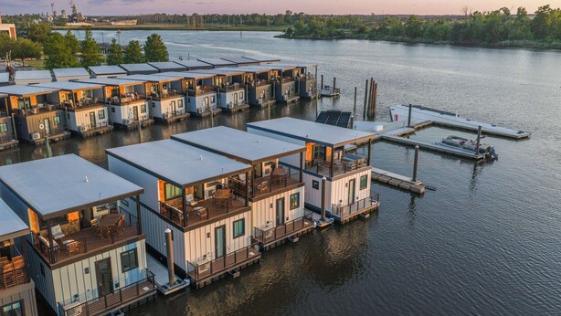 A waterfront property with floating houses connected by walkways, docked boats, and a ship in the background.