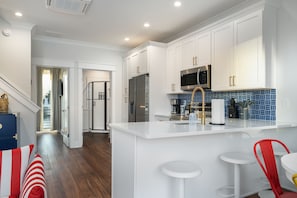 A modern kitchen with white cabinetry, stainless steel appliances, and a blue-tiled backsplash. - Newport at The Cove Riverwalk Villas (Wilmington)