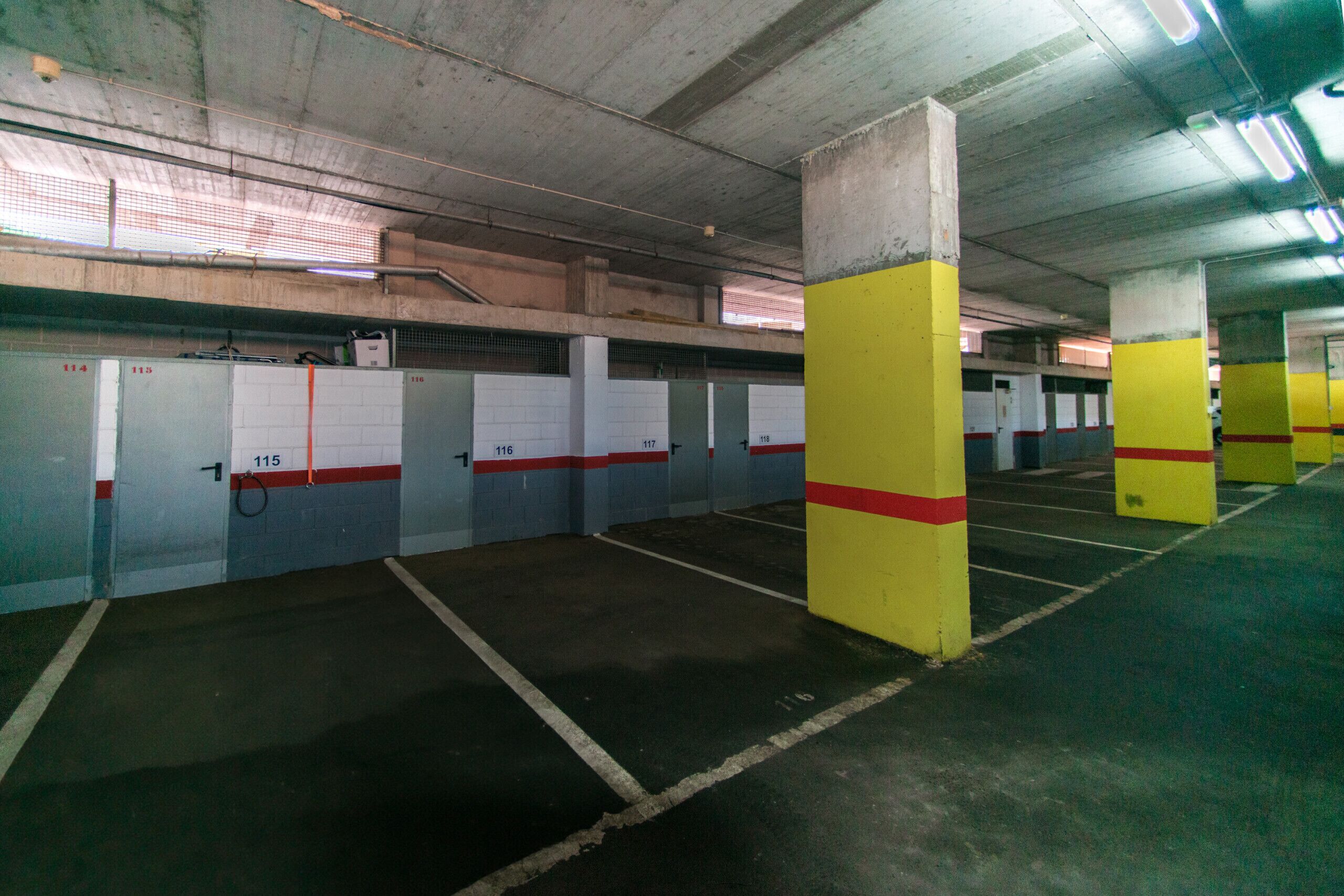 Een ondergrondse parkeergarage met betonnen pilaren, genummerde parkeerplaatsen en een metalen dak.