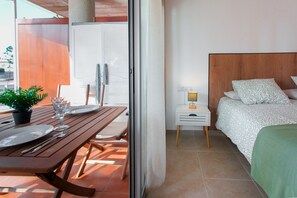 Ein Zimmer mit einem Bett, einem Nachttisch mit Lampe, einem Fenster und einem Balkon mit Tisch für zwei Personen.