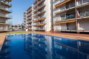 Ein modernes, mehrstöckiges Wohngebäude mit Balkonen, einem Schwimmbad und blauem Himmel.