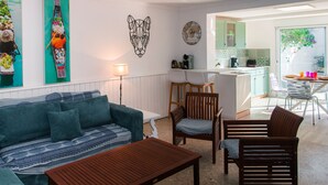 Ein Wohnzimmer mit einer Couch, einem Holztisch und Stühlen, einer Küchenzeile sowie einem Esstisch mit Stühlen.