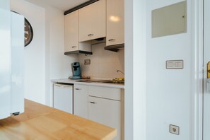 Una cocina con armarios blancos, cafetera y lavamanos.