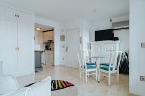 Un espacio habitable compacto con comedor, kitchenette y televisor de pantalla plana montado sobre un mueble bajo.