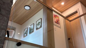 A modern interior with a wooden ceiling, glass railings, and artwork on the walls. - Modern Minimalist Cabin in quiet setting. 12-minute walk to reekside gondola. (Whistler)