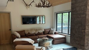 A modern living room with a stone fireplace, a large window, and a cozy seating area. - Modern Minimalist Cabin in quiet setting. 12-minute walk to reekside gondola. (Whistler)