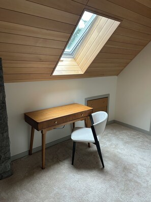 A room with a sloped ceiling, a skylight, a wooden desk, a chair, and a stone accent wall.