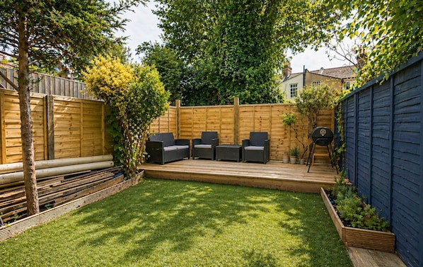 A backyard with a wooden deck, outdoor seating, and a garden bed. - Apartment Sleeps 2 With Wifi (London)