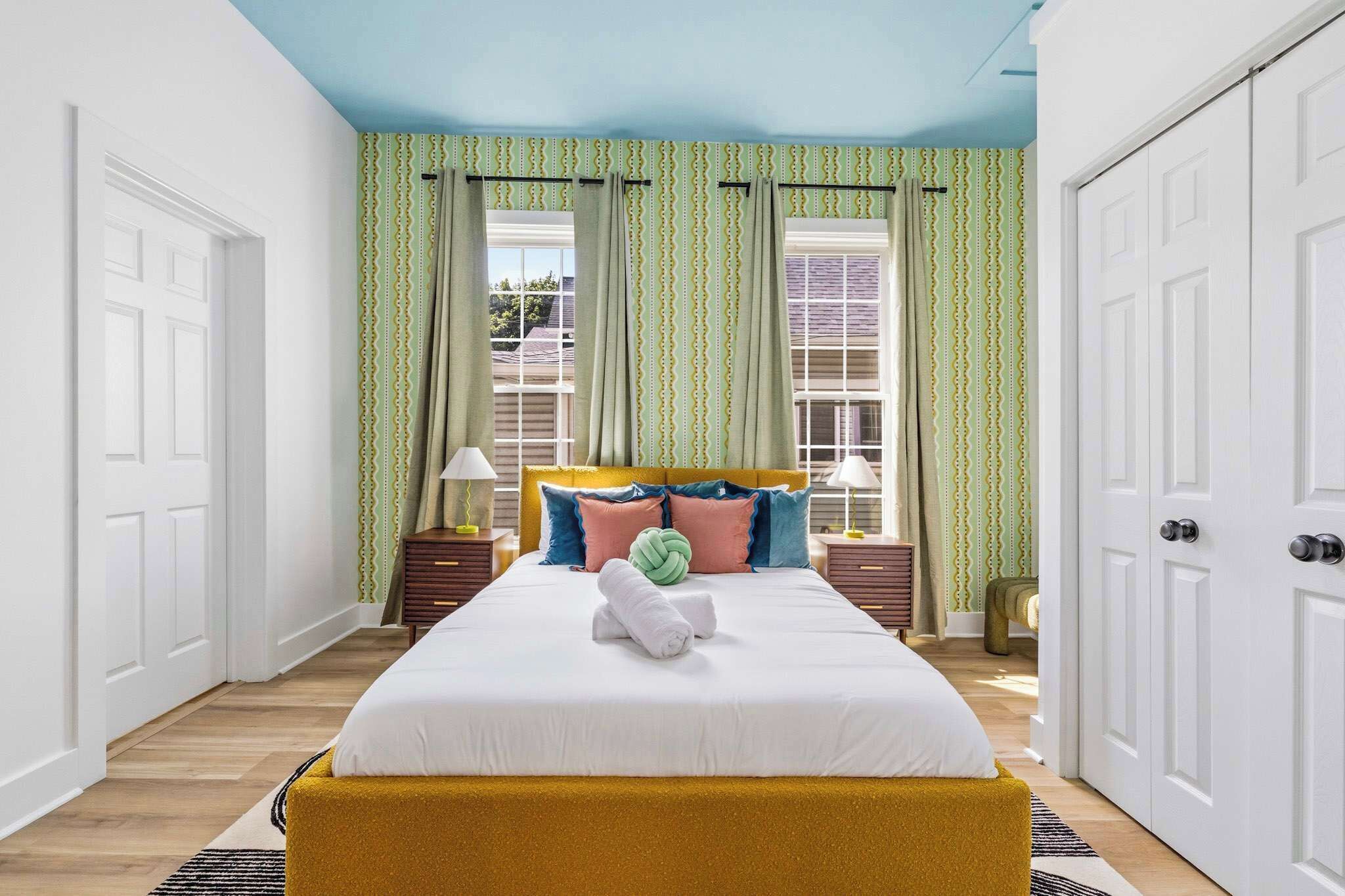 A neatly arranged bedroom with a bed, curtains, a bedside table, and a nightstand.