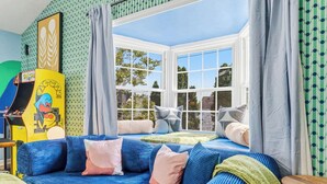 A room with a blue sofa, a window with curtains, and a wall with a patterned wallpaper. - Urban Haven Indy | Hot Tub + Game Room (Indianapolis)