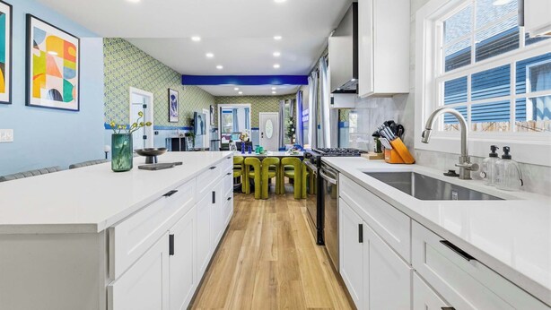 A modern kitchen with white cabinetry, a central island, and a large window. - Urban Haven Indy | Hot Tub + Game Room (Indianapolis)