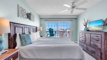 A bedroom with a bed, dresser, ceiling fan, and a view of the outside.