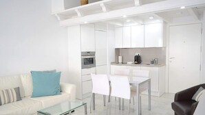 Ein modernes Wohnzimmer mit Glastisch, weißem Sofa und Essbereich mit Stühlen.