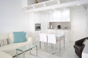 Ein modernes Wohnzimmer mit Glastisch, weißem Sofa und Essbereich mit Stühlen.