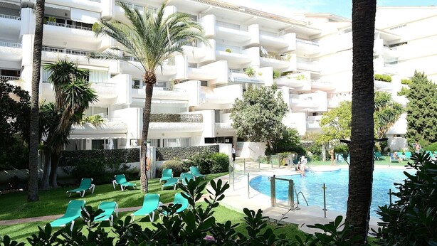 Ein mehrstöckiges Hotel mit Balkonen, einem Schwimmbecken und Grünflächen.