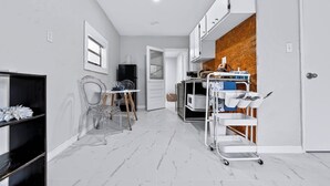 Un pasillo estrecho con una zona de cocina que cuenta con armarios blancos, un microondas y un carrito con vajilla.