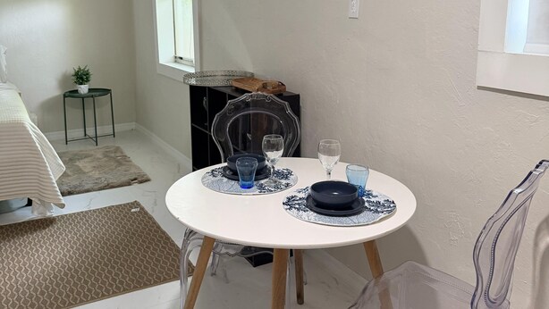 Un comedor con una mesa redonda, sillas transparentes, una mesita auxiliar y un espejo en la pared.