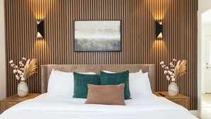 A modern bedroom with a wooden panel wall, a large bed with white and teal bedding, and two bedside tables with vases. - Pet-Friendly Branson Condo Sleeps 6~ Walk to Landing, Pools, Resort & Gym access (Branson)