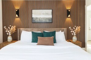 A modern bedroom with a wooden panel wall, a large bed with white and teal bedding, and two bedside tables with vases.