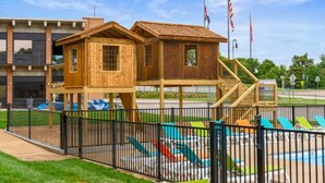 A playground with a wooden playhouse, slides, and a fenced area. - Pet-Friendly Branson Condo Sleeps 6~ Walk to Landing, Pools, Resort & Gym access (Branson)