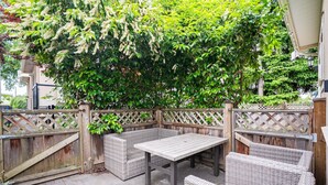 En udendørs terrasse med fletmøbler, et bord og et træhegn.
