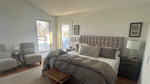 Un dormitorio con cama, dos sillas, una mesita, una mesita de noche y una ventana.