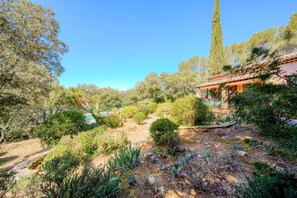 A garden with various plants and trees, a pathway, and a building with a red roof. - Lou Christalou - Avec Piscine privée (Carcès)