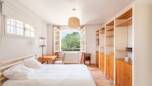 Ein Schlafzimmer mit Bett, Schreibtisch, Stuhl, Heizkörper und einem Fenster mit geöffnetem Klappladen.