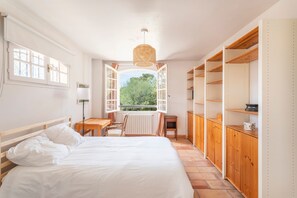 Ein Schlafzimmer mit Bett, Schreibtisch, Stuhl, Heizkörper und einem Fenster mit geöffnetem Klappladen.