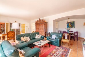 Un salón con sofás de cuero verde, un aparador de madera, una zona de comedor con una mesa y sillas, y una araña.