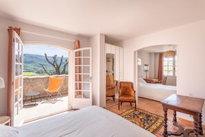 Un dormitorio con una cama grande, una silla, una mesita y vistas al exterior.
