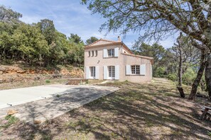Una casa de dos pisos con fachada de piedra, contraventanas blancas y entrada pavimentada.