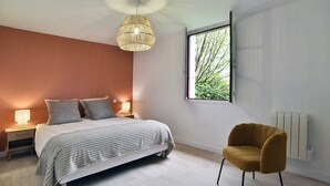 Ein Schlafzimmer mit Bett, Nachttischlampen, einem Fenster mit Blick, einem Heizkörper und einem Sessel.