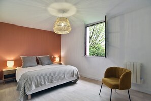 A bedroom with a bed, bedside lamps, a window with a view, a radiator, and a chair. - L'Etang Guillaume - Avec Jacuzzi, jardin de 5000m2 (Poilley)