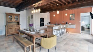 Ein Essbereich mit Holztisch, Bänken und Stühlen, eine Küche mit modernen Geräten und einer Holzbalkendecke.